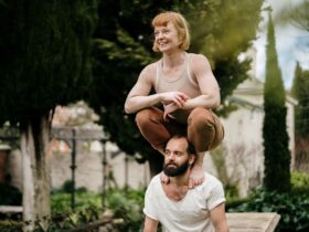 A man and a woman doing acrobatics outside. The woman is crouching on the man's shoulders.