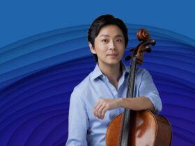 Li-Wei Qin is smiling at the camera and resting his forearm on his cello