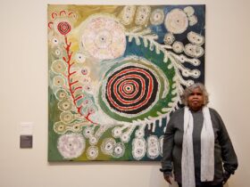 Artist Tuppy Ngintja Goodwin stands in front of her painting.
