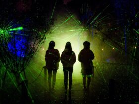 Three women walk through a natural area, surrounded by laser beams and green light.