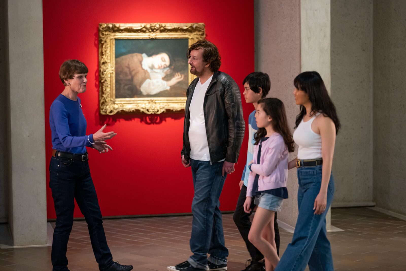 A tour guide and a family in front of a framed artwork in a gallery