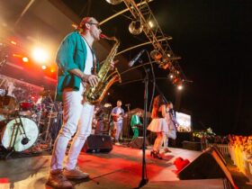 Male saxophone player performing on a colourful stage in white pants, a green shirt.