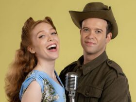 A male and female actor dressed in 1940s costumes - a solider uniform and a blue dress.
