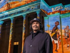 Vincent Namatjira stands in front of AGSA's facade, on the facade is Vincent's projection