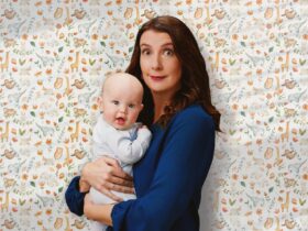Writer Anna Goldsworthy holds a baby, standing against nursery wallpaper